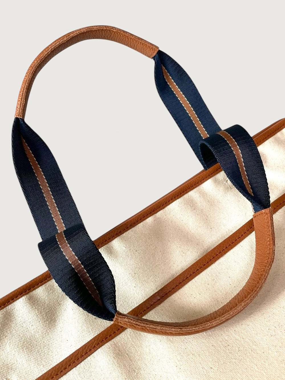 Close-up of navy and tan striped handles with leather trim on cream canvas tote bag.