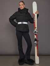 Model wearing the Bufera Ski Jacket in black, full body view holding skis with the white belt visible.