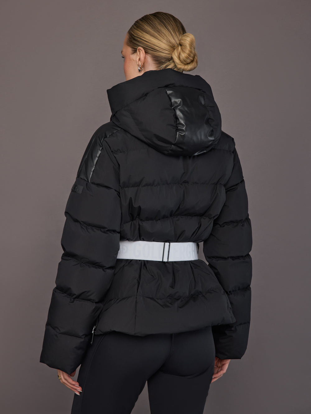 Back view of the model wearing the Bufera Ski Jacket in black, hood up and belt detail visible.