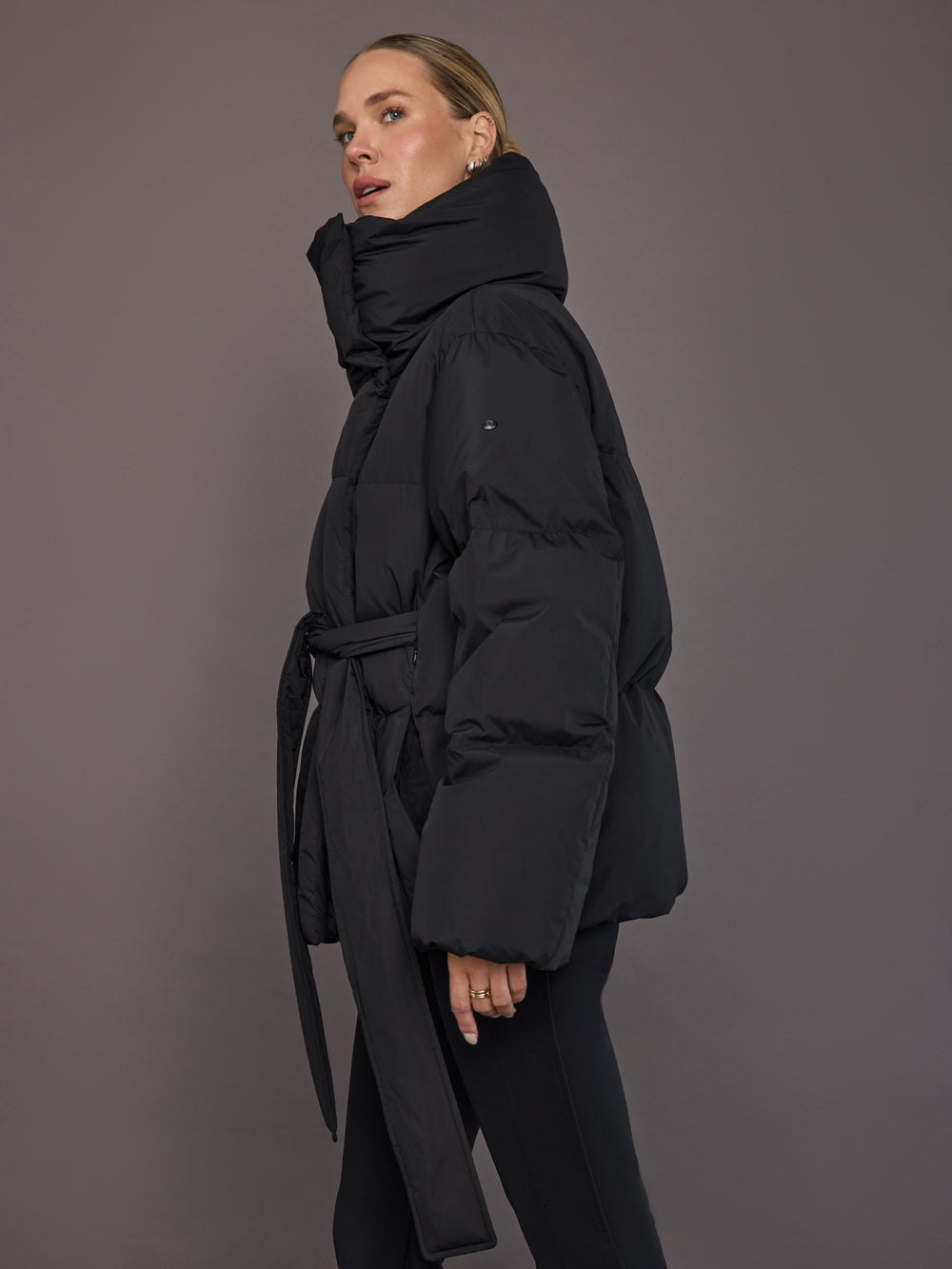 Black quilted down jacket on model, side view showing waistbelt.