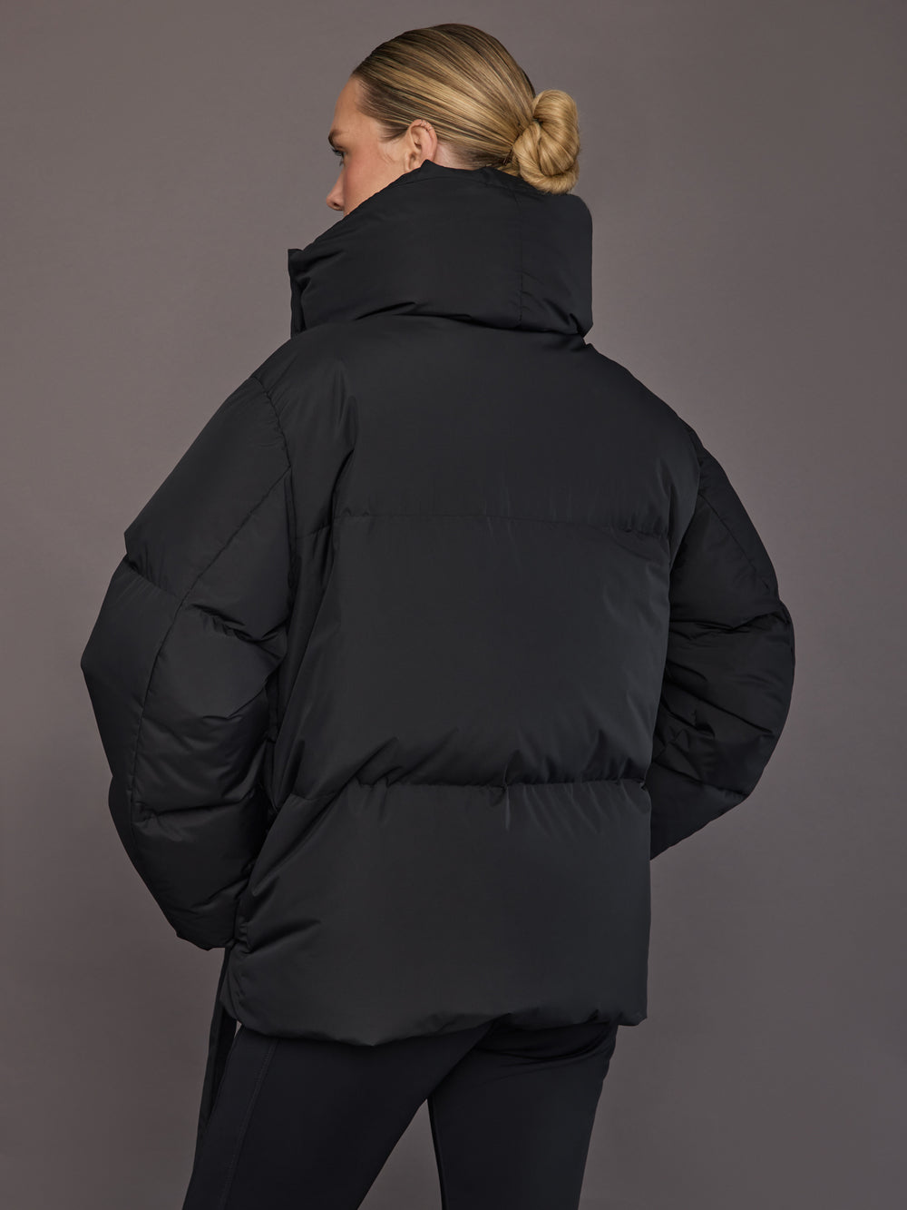 Black quilted down jacket on model, back view with tall collar.