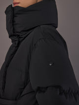 Black quilted down jacket on model, close sleeve view with logo detail.