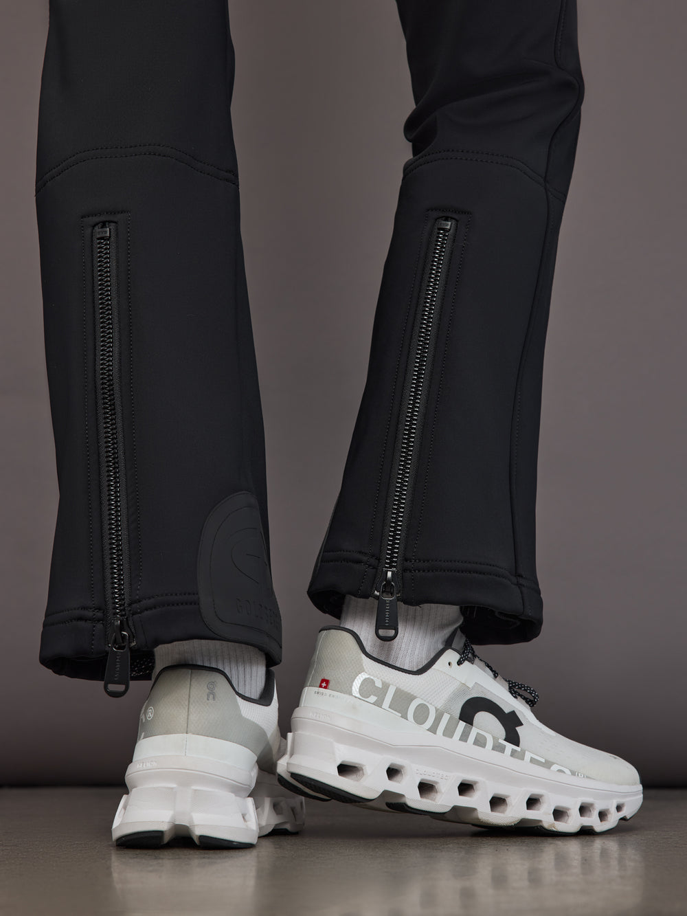 Black softshell ski pant on model, close back view of hem zippers and snowcatchers.