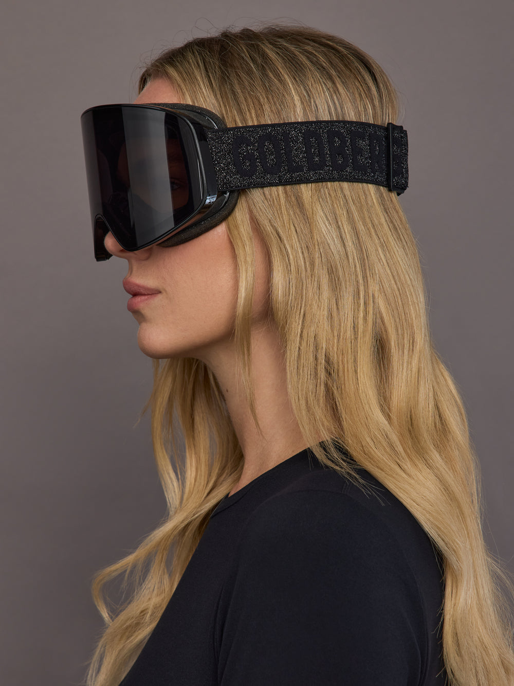 Black frameless ski goggle on model, side view showing branded strap.