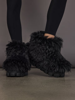 Black faux fur low snowboot on model, front angled view with crossed feet.
