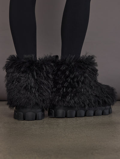 Black faux fur low snowboot on model, back view showing low shaft and faux fur texture.