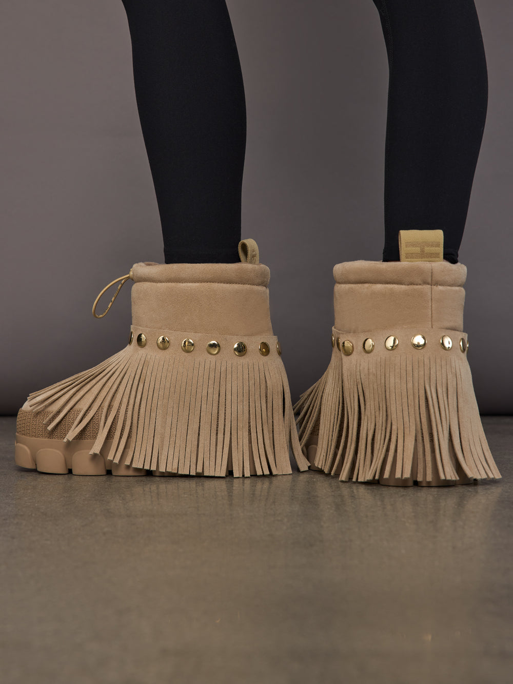 Model is wearing the Vergara Snowboot Low in Caramello, back view showing studs and fringe.
