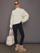 Model is wearing a cream oversized turtleneck sweater with black leggings, full body front view.