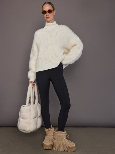 Model is wearing a cream oversized turtleneck sweater with black leggings, full body front view.