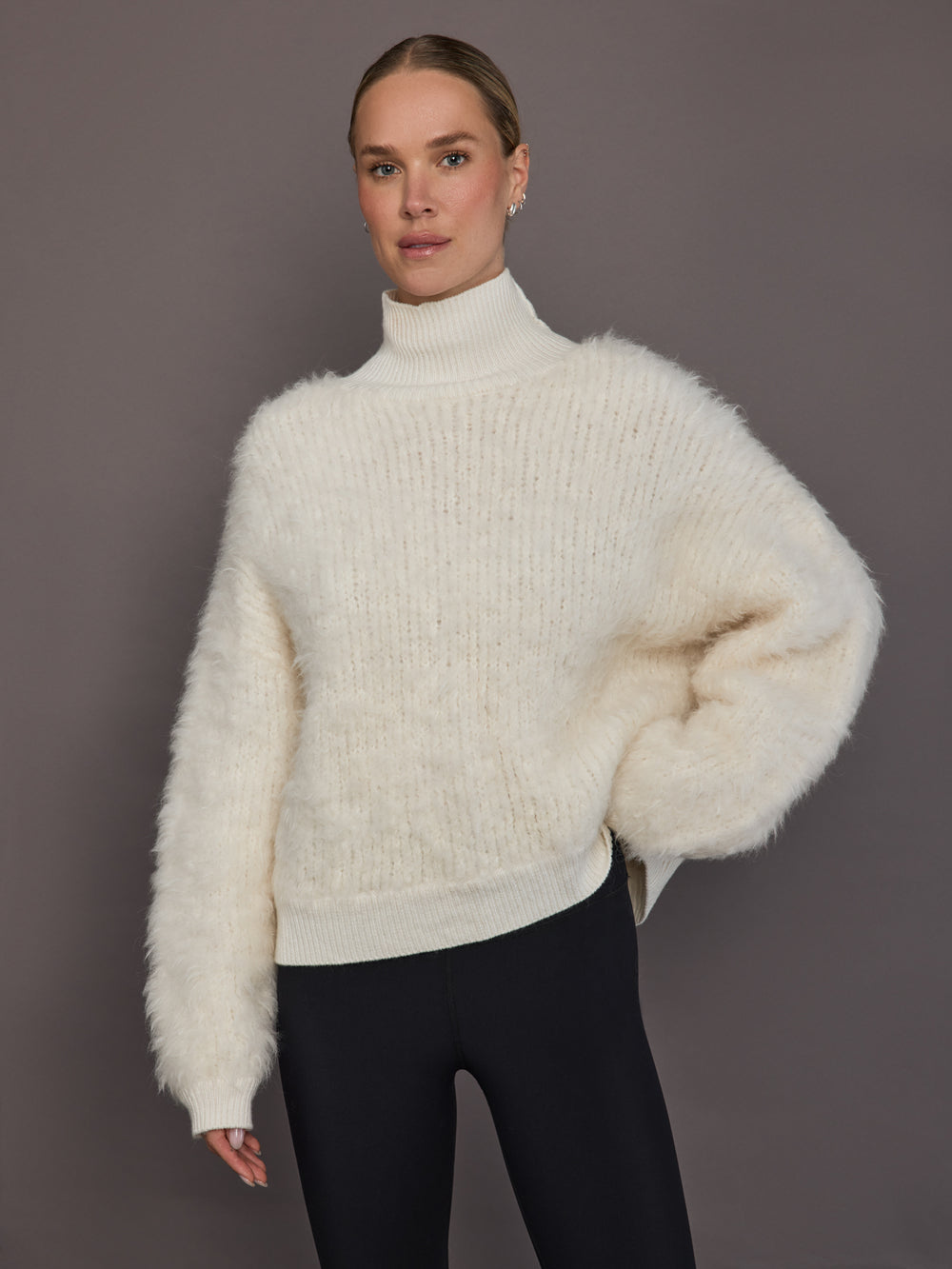 Model is wearing a cream oversized turtleneck sweater, front view showing fluffy knit texture.