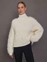 Model is wearing a cream oversized turtleneck sweater, front view showing fluffy knit texture.