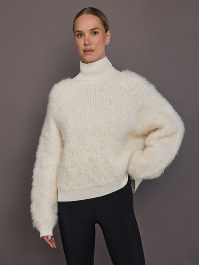 Model is wearing a cream oversized turtleneck sweater, front view showing fluffy knit texture.