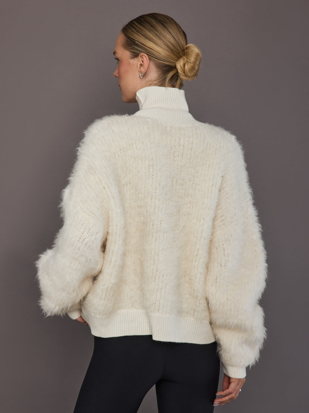 Model is wearing a cream oversized turtleneck sweater, back view showing relaxed silhouette.