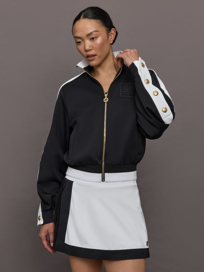 Model wears A black track jacket with white side paneling and gold zippers and snaps along forearm.