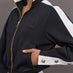 Model wears A black track jacket with white side paneling and gold zippers and snaps along forearm.
