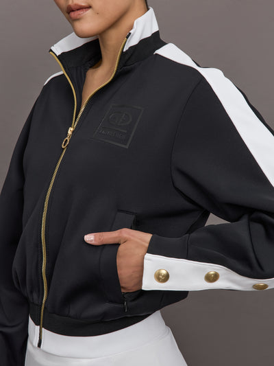Model wears A black track jacket with white side paneling and gold zippers and snaps along forearm.