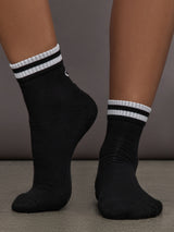 Model wears black athletic sock with contrast stripe patterning.


