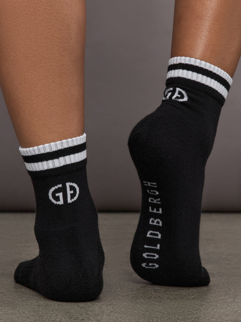 Model wears black athletic sock with contrast stripe patterning.
