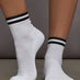 Model wears white athletic sock with contrast stripe patterning.
