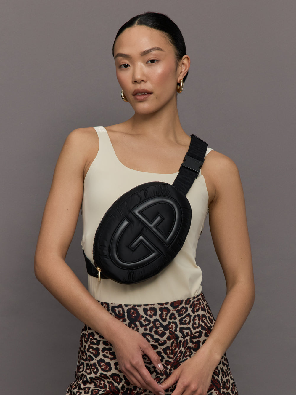 Model wears a black cross body oval bag with large leathery goldbergh logo.