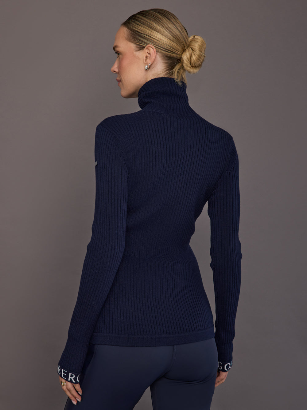 Model wearing ribbed navy turtleneck sweater, back view.