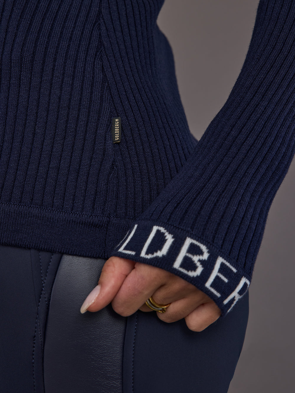 Close-up of ribbed navy turtleneck sweater, cuff and logo detail.