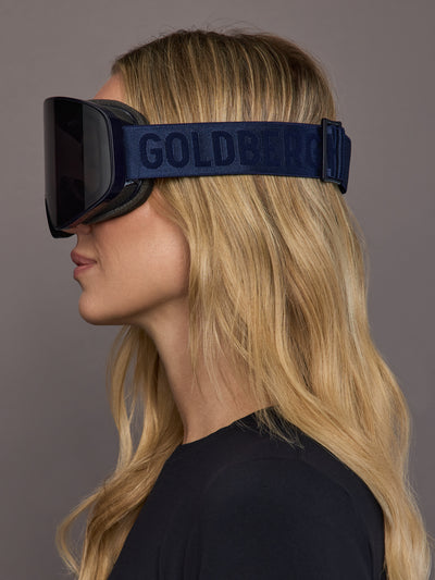 Model wearing navy ski goggles, side view showing strap detail.