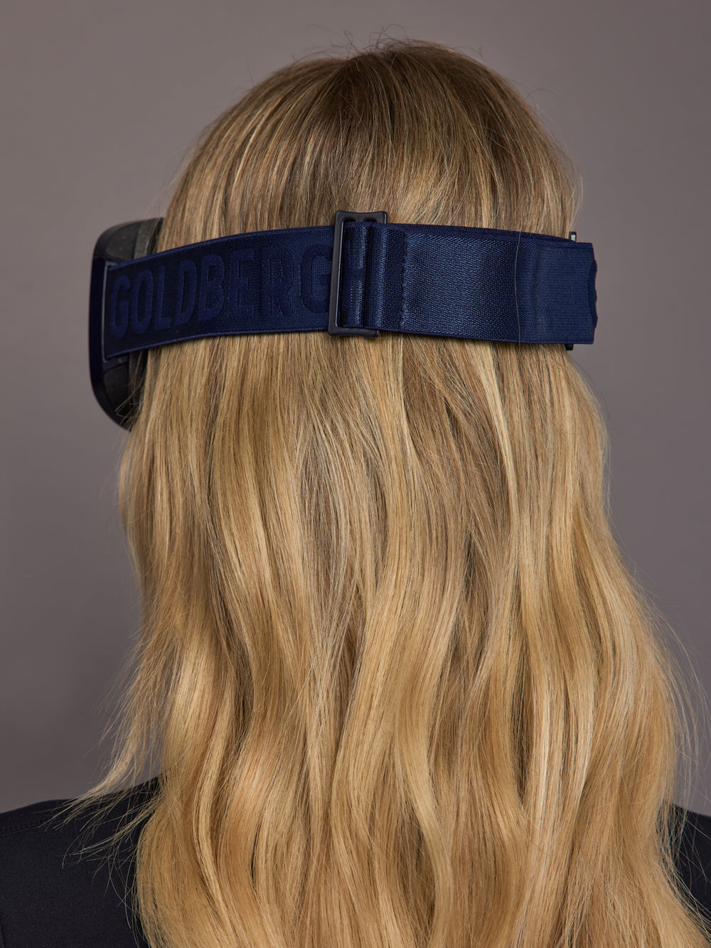 Model wearing navy ski goggles, back view with adjustable strap.