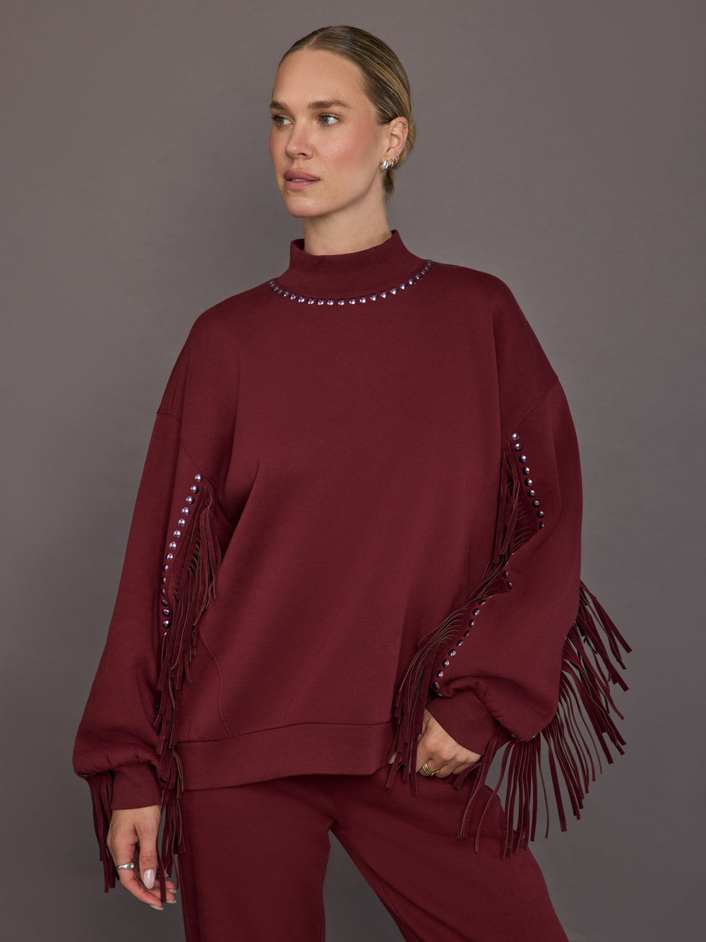 Model is wearing Frenzy Crew Neck Fringe Sweatshirt in Vino Rosso, front view.