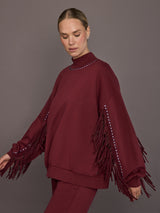 Model is wearing Frenzy Crew Neck Fringe Sweatshirt in Vino Rosso, side view showing sleeve fringe detail.