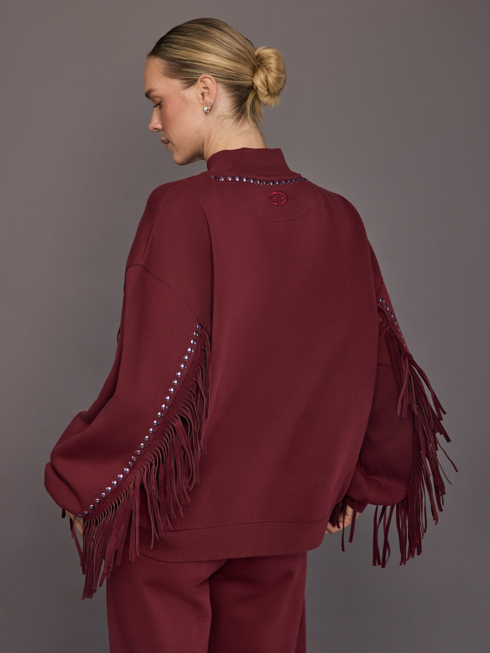 Model is wearing Frenzy Crew Neck Fringe Sweatshirt in Vino Rosso, back view with logo detail.