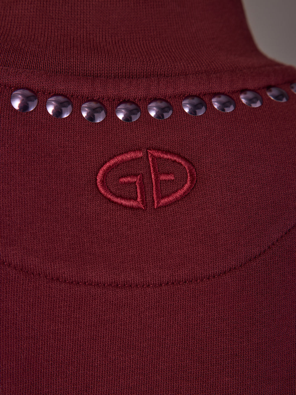 Close-up of tonal embroidered logo and stud neckline detail on Frenzy Crew Neck Fringe Sweatshirt in Vino Rosso.