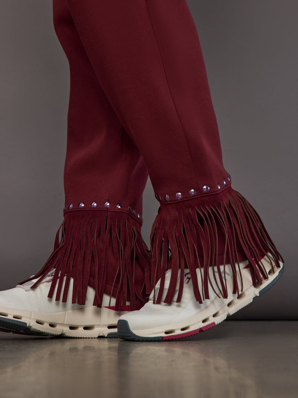 Close-up of fringe hem with stud accents on vino rosso track pants.
