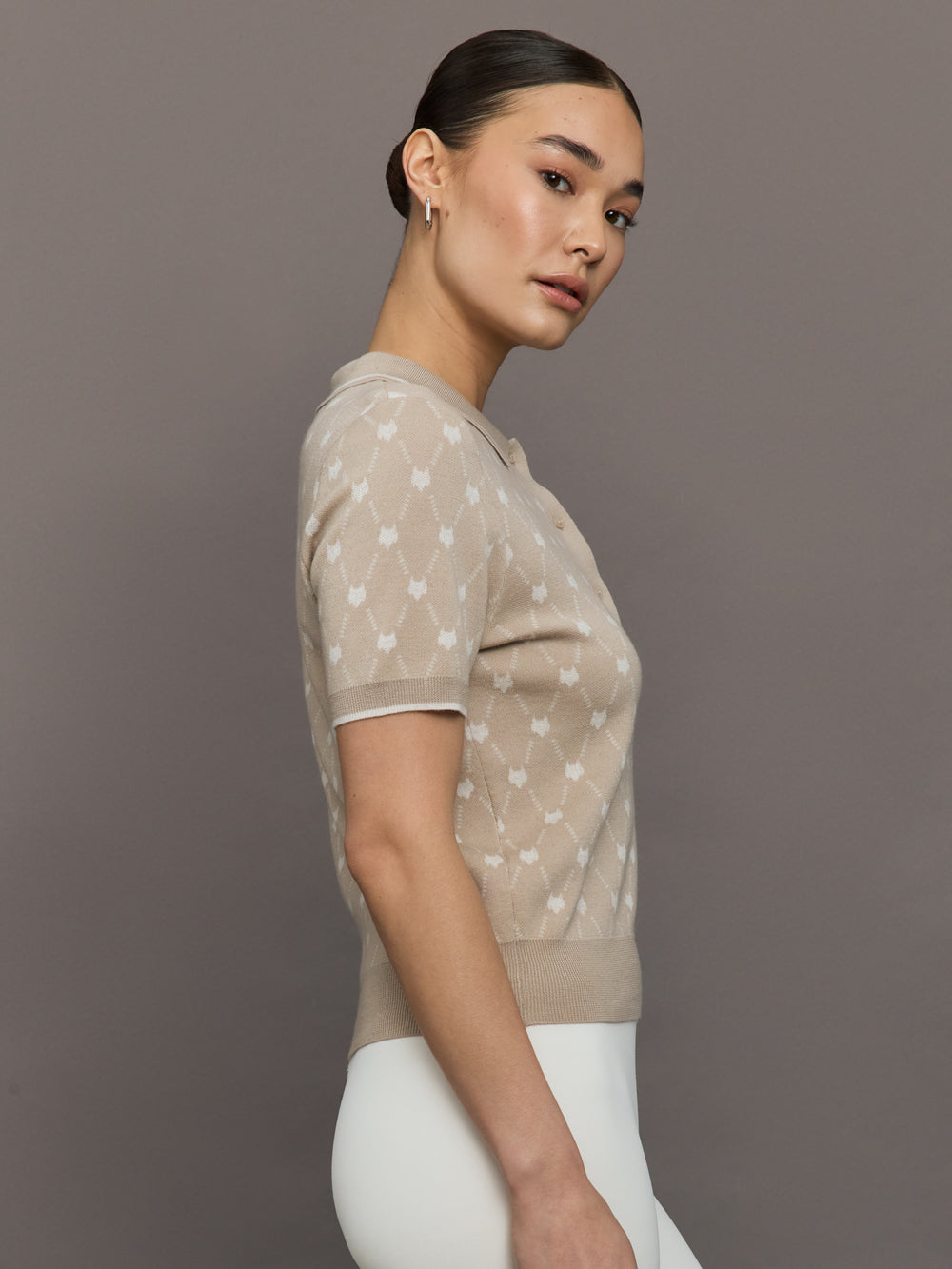 Woman wearing a beige short-sleeve top with white patterns against a brown background