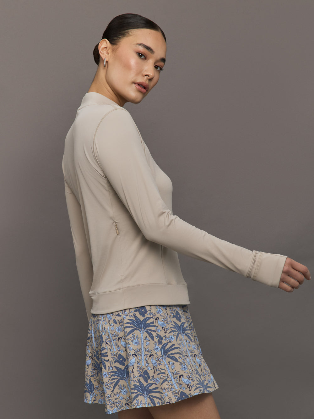 Woman wearing a beige long-sleeve top and a blue floral skirt on a gray background