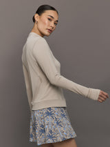 Woman wearing a beige long-sleeve top and a blue floral skirt on a gray background