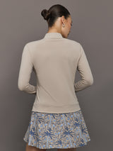 Woman wearing a beige long-sleeve top and floral skirt against a gray background