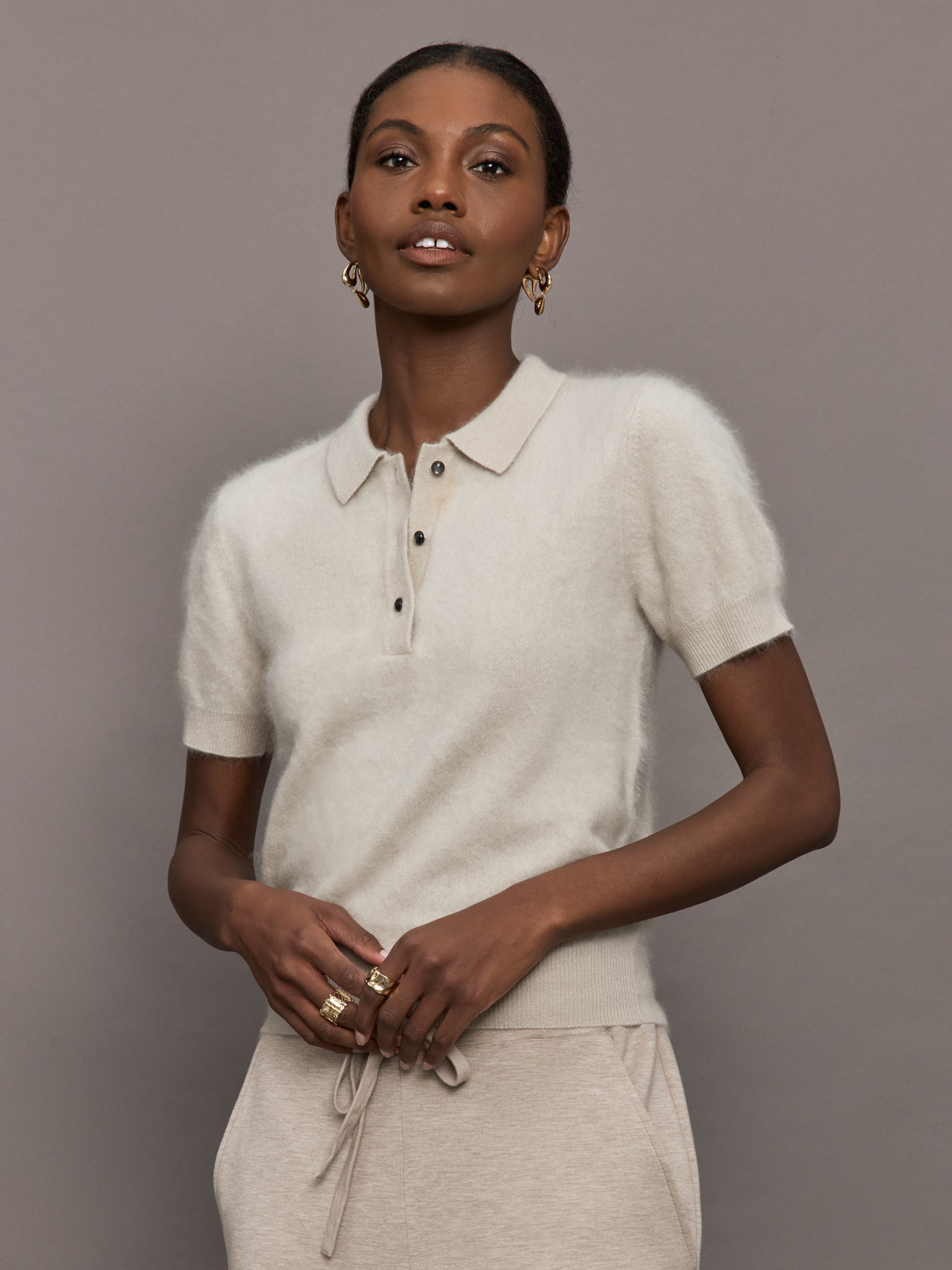 Model wears a neutral colored button up short sleeved polo sweater in a wool/cashmere blend. 