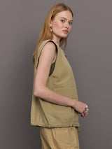 Model wears a wide shoulder, khaki zip up vest with tactical symmetrical front cargo pockets at the waist.