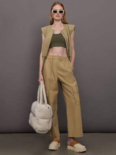 Model wears a wide shoulder, khaki zip up vest with tactical symmetrical front cargo pockets at the waist.