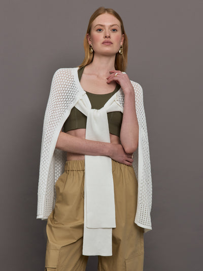 Model wears a sheer mesh white over the shoulder cape tied together at the front by sleeves. 