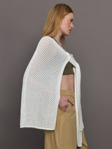 Model wears a sheer mesh white over the shoulder cape tied together at the front by sleeves. 