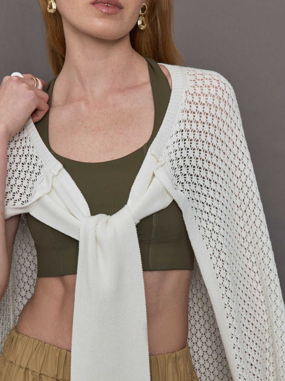 Model wears a sheer mesh white over the shoulder cape tied together at the front by sleeves. 