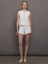 Model wears a white collared tank with chunky gold buttons and symmetrical pockets below the waist.