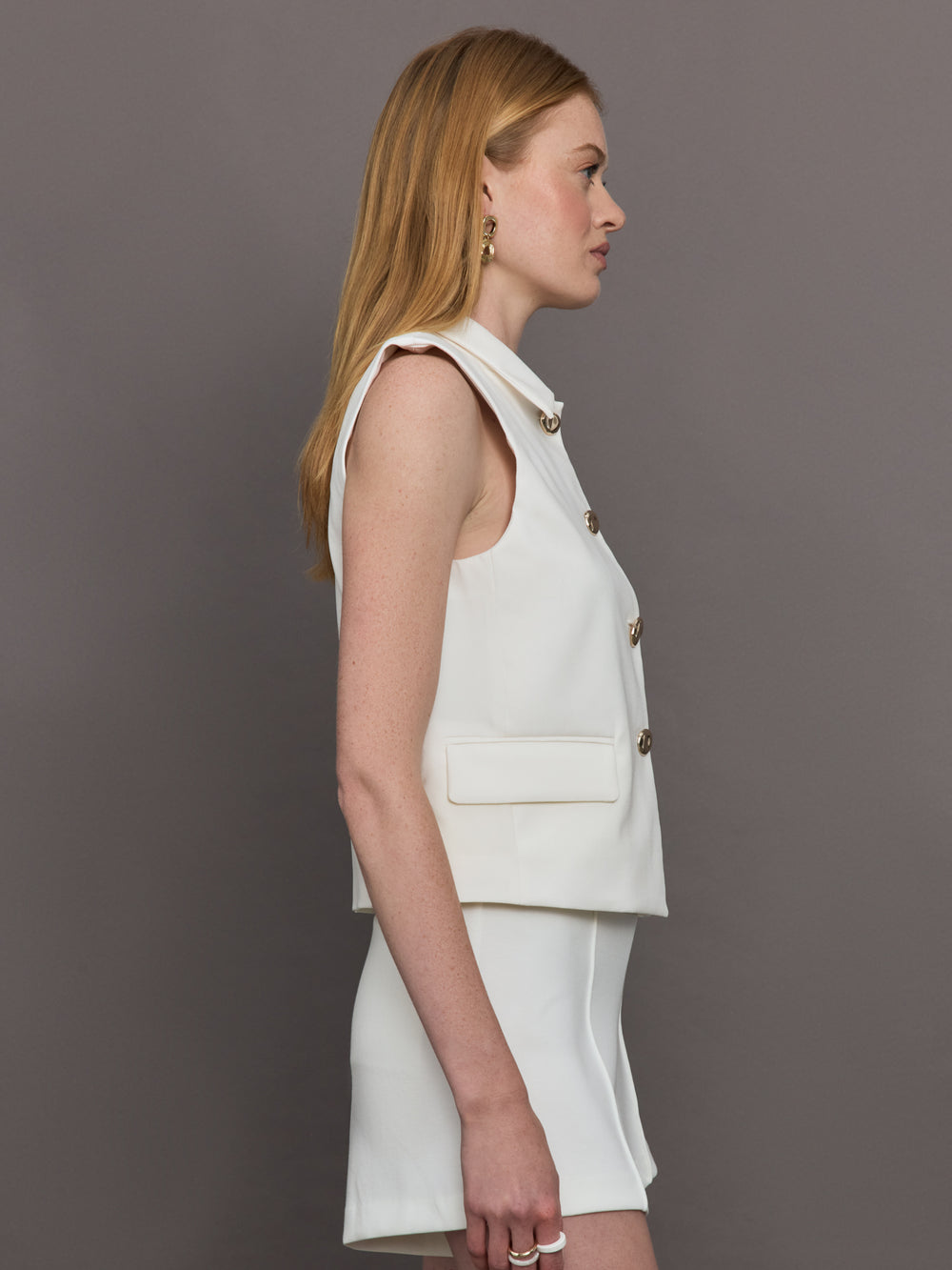 Model wears a white collared tank with chunky gold buttons and symmetrical pockets below the waist.
