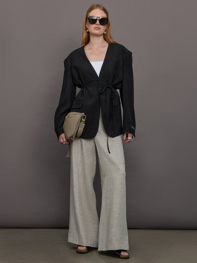 Model wears a wide shoulder black blazer with a deep v neck and drawstring closure. 