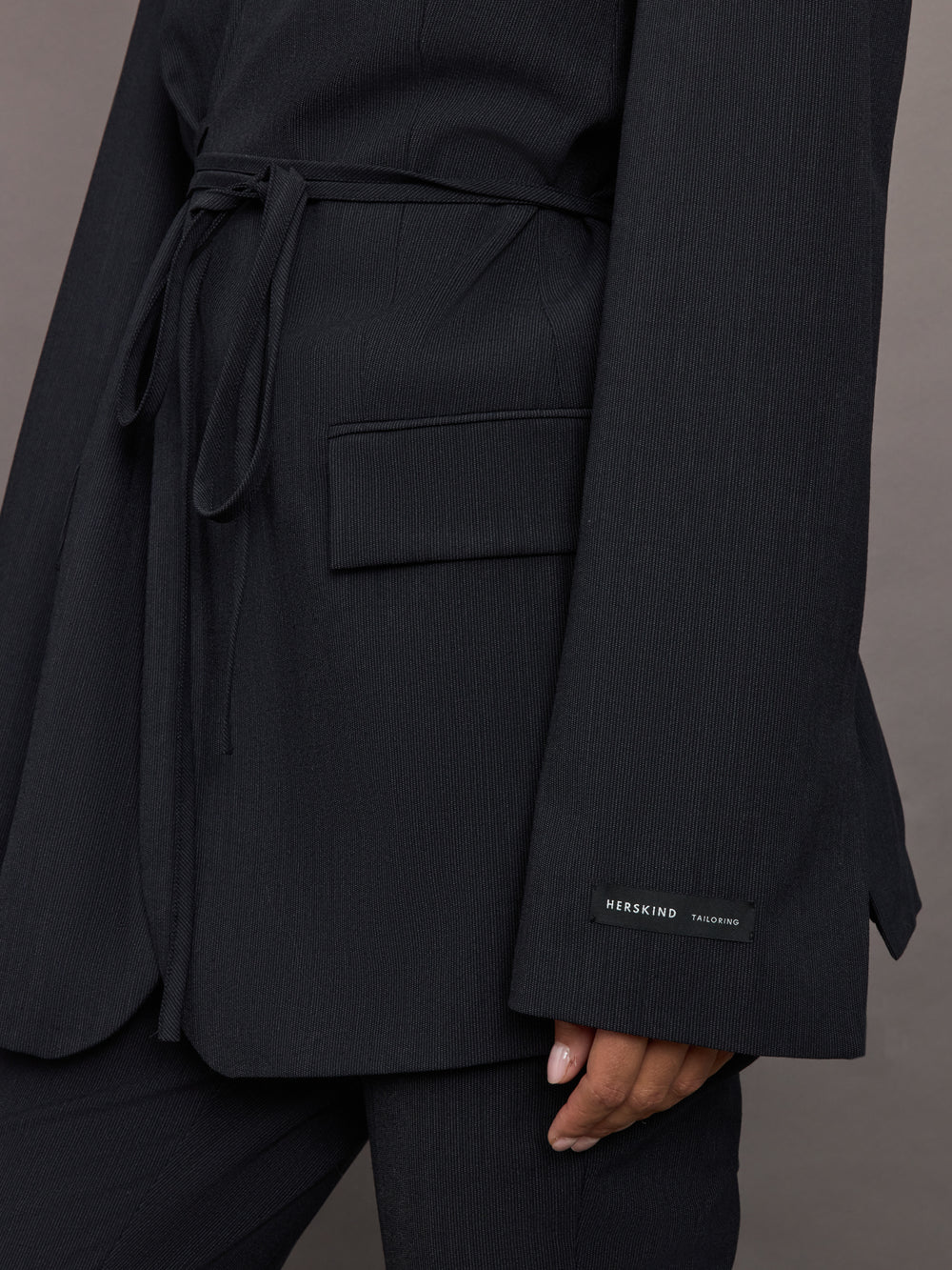 Model wearing a black blazer with a front tie.