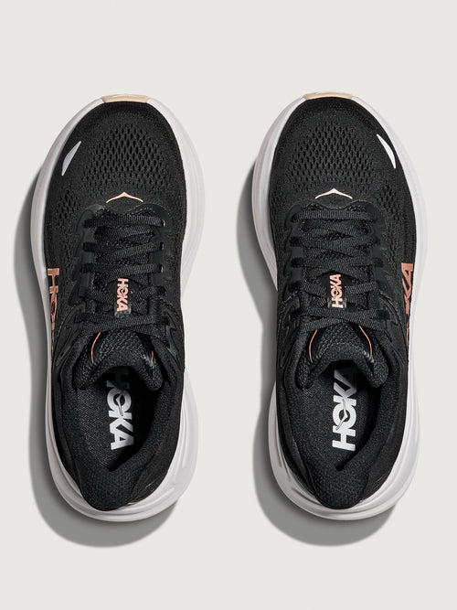 A pair of HOKA running shoes with black and rose gold color scheme.