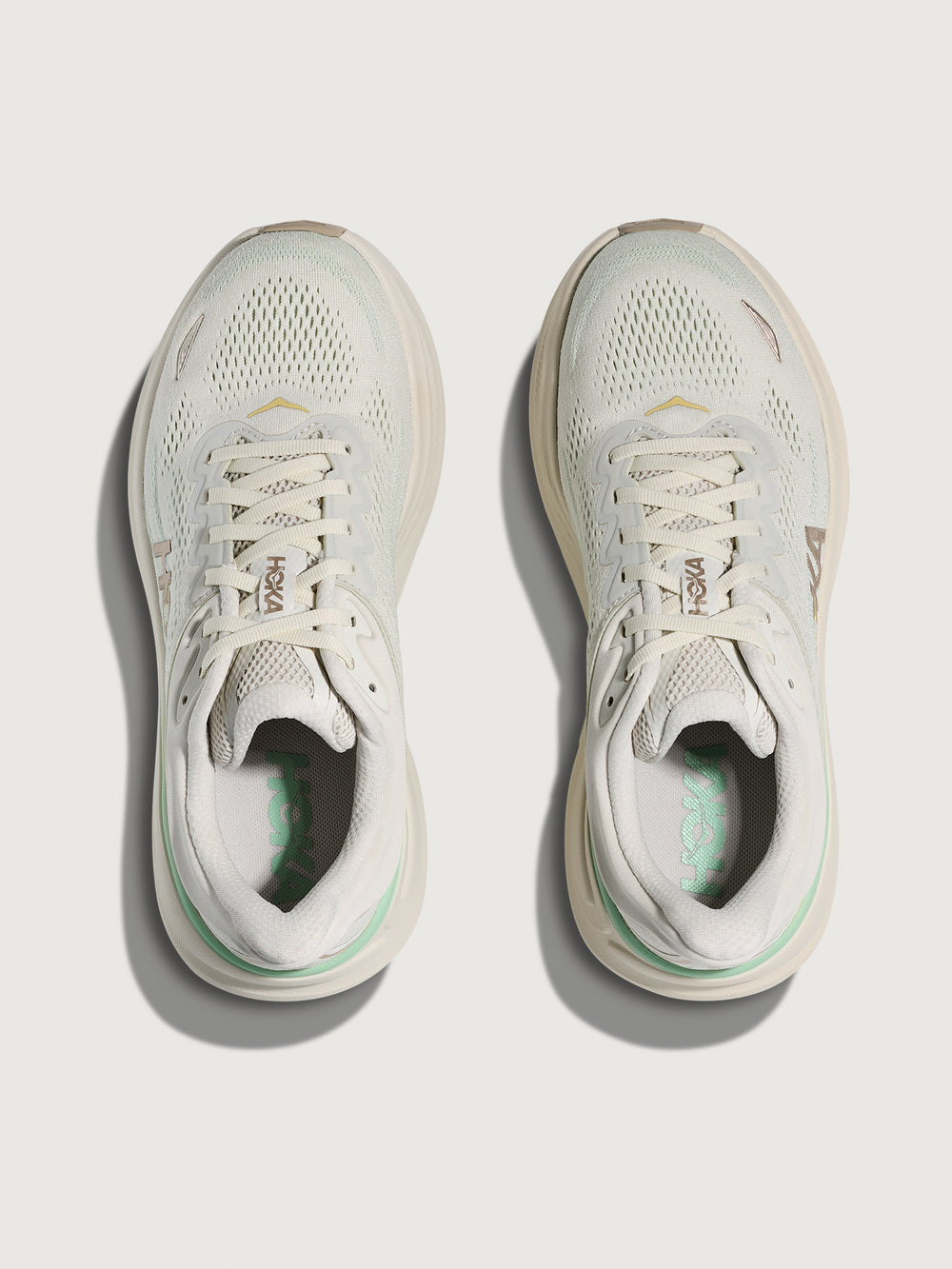 Chunky soled white Hoka running shoe with pastel green trim. 