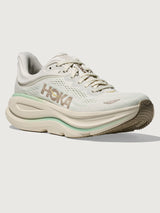Chunky soled white Hoka running shoe with pastel green trim. 